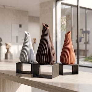 Può includere: Tre vasi a forma di goccia con texture a coste verticali, nei colori grigio chiaro, marrone scuro e terracotta. Ogni vaso è montato su un supporto rettangolare nero separato, creando un'esposizione uniforme di tre distinti recipienti.
