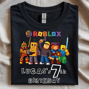 Può includere: T-shirt nero con un design Roblox colorato e personaggi dei cartoni animati. È presente anche il testo "LUCAS'S 7th BIRTHDAY". Il design è centrato sulla parte anteriore della maglietta.