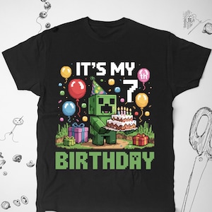 Könnte beinhalten: Schwarzes T-Shirt mit einer grünen Pixelfigur, die einen Geburtstagskuchen mit Kerzen hält. Der Text "It's My 7th Birthday" ist auf dem Shirt aufgedruckt.