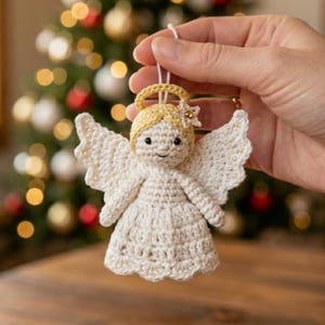 May include: A handmade crochet angel Christmas ornament. The angel has a cream-colored body, wings, and halo, with a golden star on its head. The angel is held up by a white string, ready to hang on a Christmas tree.