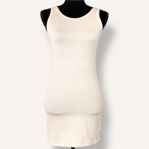 May include: A cream-colored tank dress displayed on a black mannequin. The dress is sleeveless with a scoop neckline and a fitted silhouette that extends to the mid-thigh. The fabric appears to be a soft, knit material.