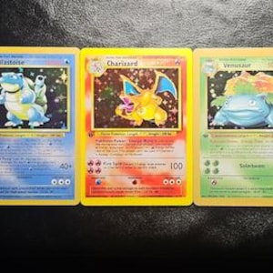 May include: Three rectangular trading cards featuring Blastoise, Charizard, and Venusaur. Each card displays a holographic illustration of the character, text detailing abilities, and a yellow border. The cards are arranged side-by-side.