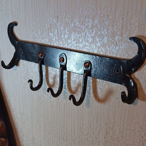 May include: Black metal coat rack with five hooks. The hooks are curved and have a decorative design. The rack is mounted on a wall.