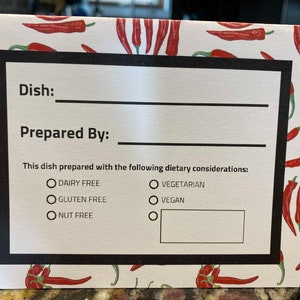 Può includere: Biglietto di ricetta con sfondo bianco e motivo a peperoncino rosso. La carta ha un bordo nero e include campi per "Piatto" e "Preparato da". Le considerazioni dietetiche includono senza latticini, senza glutine, senza noci, vegetariano e vegano.
