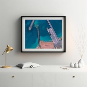 Peut inclure: Vue aérienne d'un port avec une jetée qui s'étend dans l'eau. L'eau est d'un bleu éclatant et la jetée est de couleur gris clair. Un petit bateau est amarré à la jetée.