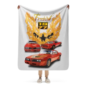 Könnte beinhalten: Eine weiße Fleece-Decke mit einem roten 1977 Pontiac Trans Am Auto darauf gedruckt. Das Auto ist von Flammen umgeben und der Text "Freebird" ist über dem Auto gedruckt.