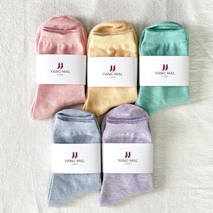 Könnte beinhalten: Fünf Paar Socken in verschiedenen Pastellfarben, darunter Rosa, Gelb, Hellgrün, Hellblau und Lavendel. Jedes Paar hat ein weißes Etikett mit dem Text "YANG MAL K socks" in Schwarz.