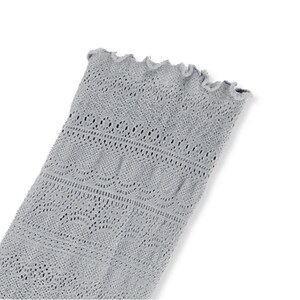 May include: A light gray, open-weave textile with a scalloped edge. The fabric has a delicate, lacy pattern with various geometric shapes and lines. The textile is likely a sleeve or part of a garment.