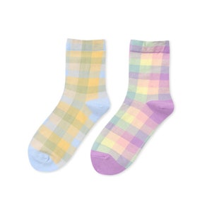 Puede incluir: Un par de calcetines a cuadros pastel. Un calcetín es azul claro con cuadros amarillos y verdes, el otro es morado con cuadros rosas y verdes.