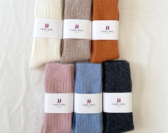 May include: Six pairs of ribbed socks in various colors, including white, beige, orange, pink, blue, and gray. Each pair has a white label with the text "YANG MAL" in black.