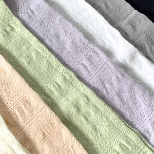May include: A collection of pastel-colored, open-weave fabric swatches arranged diagonally. The colors include light peach, green, lavender, white, gray, and navy. The fabric has a delicate, lacy pattern, creating a textured appearance. Ideal for textile projects.