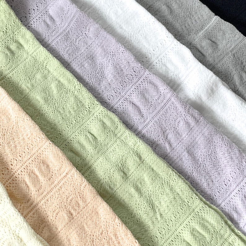 May include: A collection of pastel-colored, open-weave fabric swatches arranged diagonally. The colors include light peach, green, lavender, white, gray, and navy. The fabric has a delicate, lacy pattern, creating a textured appearance. Ideal for textile projects.