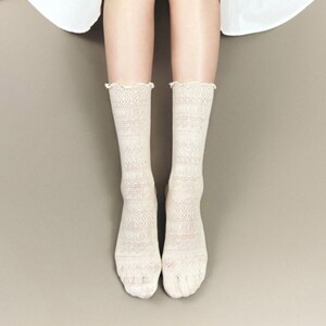 May include: A pair of off-white lace socks with a scalloped edge. The socks have a detailed, openwork pattern and are knee-high in length. The socks are made of a soft, delicate material.