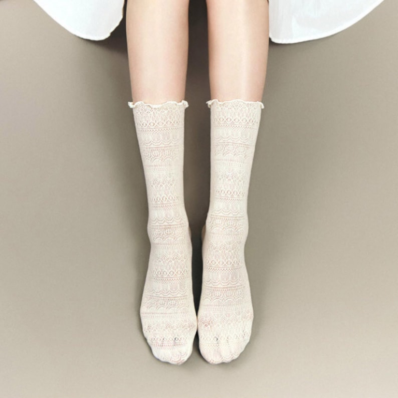 May include: A pair of off-white lace socks with a scalloped edge. The socks have a detailed, openwork pattern and are knee-high in length. The socks are made of a soft, delicate material.