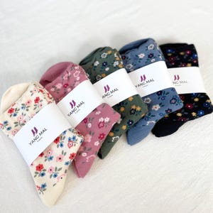 May include: Five pairs of socks with floral patterns. Each pair has a white label with the text "YANG MAL & Socks". The socks are in the colors cream, pink, green, blue, and black.