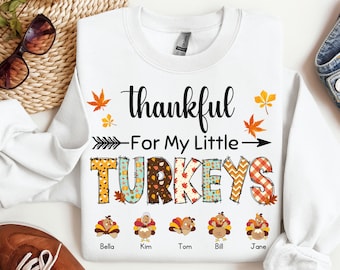 May include: White sweatshirt with the text "thankful - For My Little TURKEYS" in black. The word "TURKEYS" is made up of individual turkeys with different patterns. Below the word "TURKEYS" are five turkeys with the names Bella, Kim, Tom, Bill, and Jane.