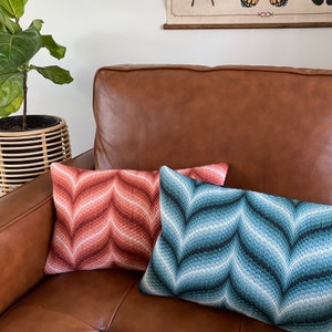 Op de afbeelding: Twee decoratieve kussens met geometrische patronen. Het kussen aan de linkerkant is rood en oranje met een chevron-patroon. Het kussen aan de rechterkant is blauw en wit met een chevron-patroon.
