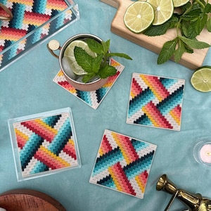 May include: A collection of square coasters featuring a vibrant geometric design in red, yellow, teal, and black. The coasters are made from a woven material. A matching tray is also present, alongside a copper mug and lime slices.