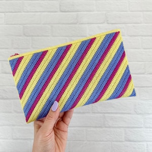 May include: A yellow and purple striped clutch purse with a diagonal pattern.