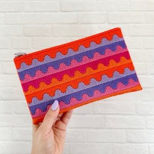 May include: A colourful zippered pouch with a wavy pattern in shades of purple, pink, orange, and red.