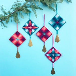 May include: Five handmade Christmas decorations with geometric patterns in shades of pink, blue, and teal. Each decoration has a gold tassel.