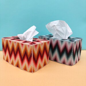 May include: Two tissue box covers with a geometric chevron pattern. One cover is red, orange, and brown, and the other is gray, black, and white.