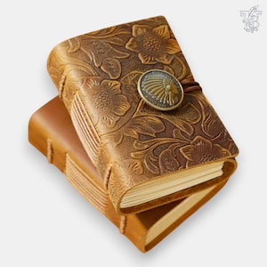 Op de afbeelding: Twee gestapelde bruin lederen tijdschriften. Het bovenste tijdschrift heeft reliëf bloemmotieven en een metalen sluiting met een embleem. Het onderste tijdschrift is effen, lichtbruin. De tijdschriften zijn gebonden met zichtbare stiksels.