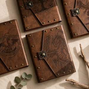 May include: Three brown journals with textured covers featuring embossed dragon and tree designs. Each rectangular notebook has a flap closure secured with a decorative metal stud and small brass-toned rivets along the edges of the cover.
