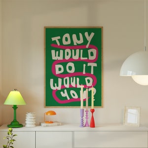 Può includere: Un poster verde con testo bianco che recita "Tony would do it would you?" su una linea rosa ondulata. Il poster è appeso a una parete bianca sopra una cassettiera bianca con una lampada verde, una pila di sottobicchieri bianchi e una piccola lampada arancione. Ci sono tre candelabri con candele gialle sulla cassettiera.