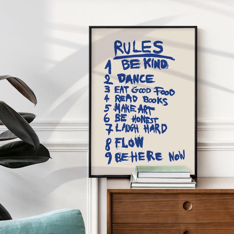 A handwritten-style poster titled “RULES,” featuring a list of nine life reminders in bold blue brush lettering on a soft beige background. The rules include: Be Kind, Dance, Eat Good Food, Read Books, Make Art, Be Honest, Laugh Hard, Flow, and Be Here Now. The expressive strokes and casual typography give the artwork a motivational, energetic, personal feel, making it an uplifting piece for homes, studios, or creative spaces.