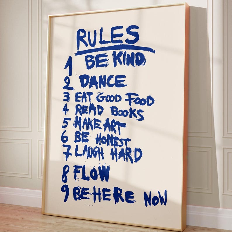 A handwritten-style poster titled “RULES,” featuring a list of nine life reminders in bold blue brush lettering on a soft beige background. The rules include: Be Kind, Dance, Eat Good Food, Read Books, Make Art, Be Honest, Laugh Hard, Flow, and Be Here Now. The expressive strokes and casual typography give the artwork a motivational, energetic, personal feel, making it an uplifting piece for homes, studios, or creative spaces.