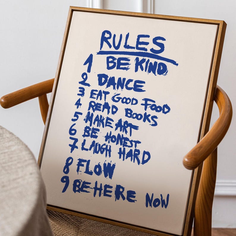 A handwritten-style poster titled “RULES,” featuring a list of nine life reminders in bold blue brush lettering on a soft beige background. The rules include: Be Kind, Dance, Eat Good Food, Read Books, Make Art, Be Honest, Laugh Hard, Flow, and Be Here Now. The expressive strokes and casual typography give the artwork a motivational, energetic, personal feel, making it an uplifting piece for homes, studios, or creative spaces.