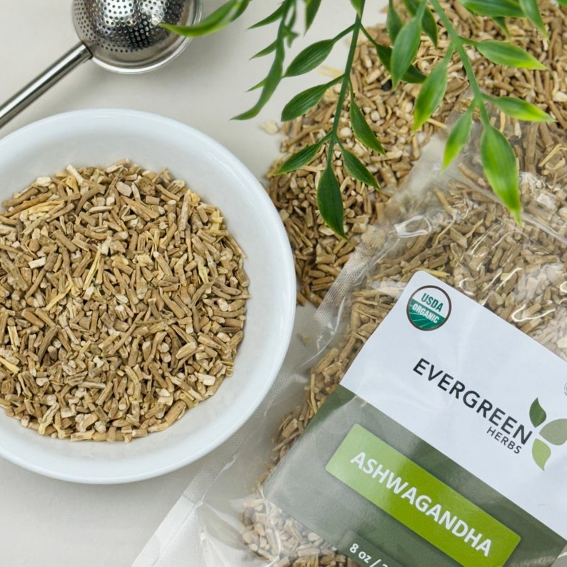 Puede incluir: Primer plano de una bolsa de ra&iacute;z de ashwagandha seca, etiquetada como "EVERGREEN HERBS" y "USDA ORGANIC". La bolsa est&aacute; abierta, revelando las piezas de ra&iacute;z seca de color marr&oacute;n claro.