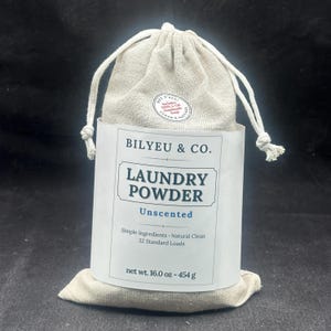Puede incluir: Una bolsa de tela beige con cord&oacute;n que contiene detergente en polvo, con una etiqueta de papel blanco que dice BILYEU & CO. LAUNDRY POWDER Unscented, Simple Ingredients, Natural Clean, 32 Standard Loads, net wt. 16.0 oz - 454 g y una pegatina.