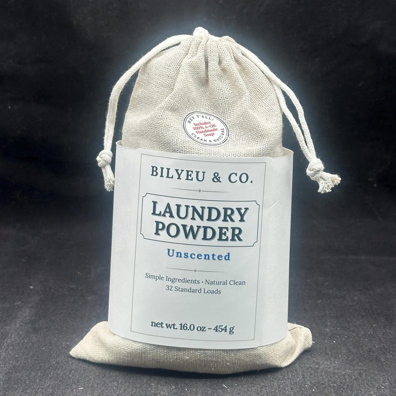 Puede incluir: Una bolsa de tela beige con cord&oacute;n que contiene detergente en polvo, con una etiqueta de papel blanco que dice BILYEU & CO. LAUNDRY POWDER Unscented, Simple Ingredients, Natural Clean, 32 Standard Loads, net wt. 16.0 oz - 454 g y una pegatina.
