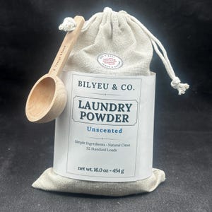 Puede incluir: Una bolsa de tela beige con cord&oacute;n de detergente en polvo Bilyeu & Co. con una etiqueta blanca que dice Laundry Powder Unscented, Simple Ingredients, Natural Clean, 32 Standard Loads, 454 g, y una cuchara de madera marcada con 15ml.