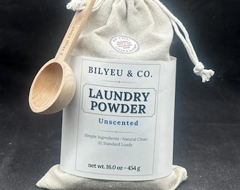May include: A beige drawstring fabric pouch of Bilyeu & Co. laundry powder with a white label reading Laundry Powder Unscented, Simple Ingredients, Natural Clean, 32 Standard Loads, net wt. 16.0 oz - 454 g, and a wooden scoop marked 1 Tbsp 15ml.