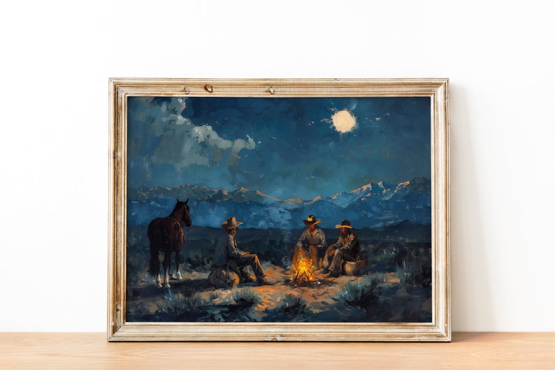 May include: A framed painting depicting a nighttime scene with four cowboys gathered around a campfire under a full moon. The cowboys are wearing hats and sitting on the ground. A horse stands behind them. The painting is set against a backdrop of mountains and a starry sky.