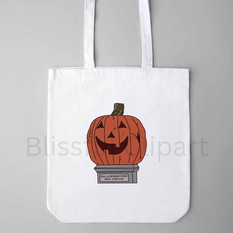 Op de afbeelding: Witte tote bag met een afbeelding van een grote oranje jack-o'-lantern met een gesneden glimlachend gezicht. De pompoen staat op een voetstuk met de tekst "HALLOWEENTOWN ESTD. LONG AGO".
