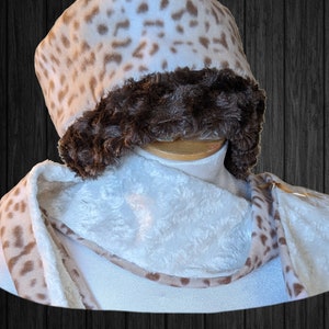 May include: A white and brown leopard print fleece hat with a brown faux fur trim. The hat is paired with a white fleece scarf with a brown leopard print trim.