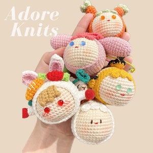 May include: A collection of five crocheted plushies in various colors and designs. The plushies are all handmade and feature unique facial expressions. The plushies are arranged in a hand, with the largest plushie in the center.