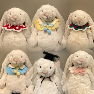 Puede incluir: Seis conejos de peluche blancos que llevan diferentes collares de ganchillo. Los collares están decorados con varios colores y patrones, incluyendo rojo, blanco, azul, amarillo y verde.
