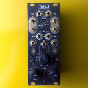 May include: A black Umbra modular synthesizer module with gold accents and various knobs and jacks. The module features the text "Umbra", "Send", "Rtrn", "In", "Feed", "Imbue", and "Drain". The module is set against a bright yellow background.