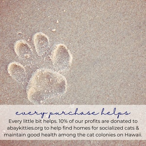 K&ouml;nnte beinhalten: Ein Pfotenabdruck im Sand mit dem Text "every purchase helps" und dem Text "Every little bit helps. 10% of our profits are donated to abaykitties.org to help find homes for socialized cats & maintain good health among the cat colonies on Hawaii."