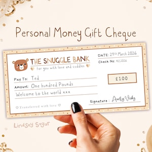 Op de afbeelding: Een gepersonaliseerde cadeaubon met de tekst "Personal Money Gift Cheque" en "The Snuggle Bank". De cheque is bestemd voor "Ted" voor "One hundred Pounds". De datum is 29 maart 2026. Handtekening "Aunty Vicky".