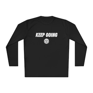 May include: Black long-sleeve shirt with the text "KEEP GOING" in white block letters across the chest. Below the text is a small circular graphic with the word "MEIVE" in a circle. The shirt is made of a smooth, likely athletic material.