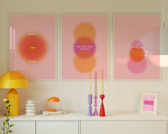 Peut inclure: Trois affiches dégradées rose et orange avec du texte motivant sur un mur blanc. Les affiches disent "protégez votre paix", "l'amour de soi, bébé, l'amour de soi" et "c'est déjà à vous". Il y a trois chandeliers avec des bougies sur une étagère blanche sous les affiches.