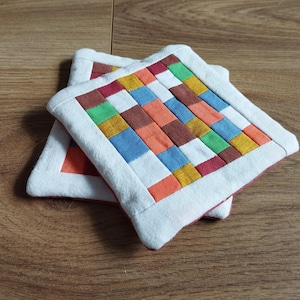 Pode incluir: Dois tapetes quadrados de tecido com uma borda branca. Os tapetes são feitos de tecido patchwork em várias cores, incluindo vermelho, laranja, amarelo, verde, azul e marrom.