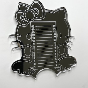 May include: A black acrylic nail art sizing guide in the shape of Hello Kitty. The guide features a series of horizontal lines with numbers from 1 to 15, used for measuring nail sizes. The design includes Hello Kitty's iconic bow and face.