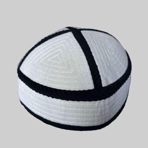 May include: White and black skullcap with a geometric design. The hat features a white base with black trim around the base and a black cross design on top. The hat is made of a soft, textured material.